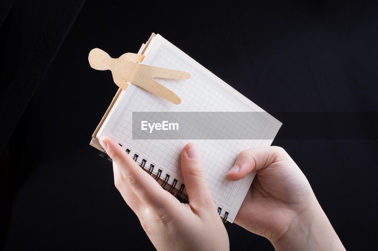 Cropped hand of person holding book against black background