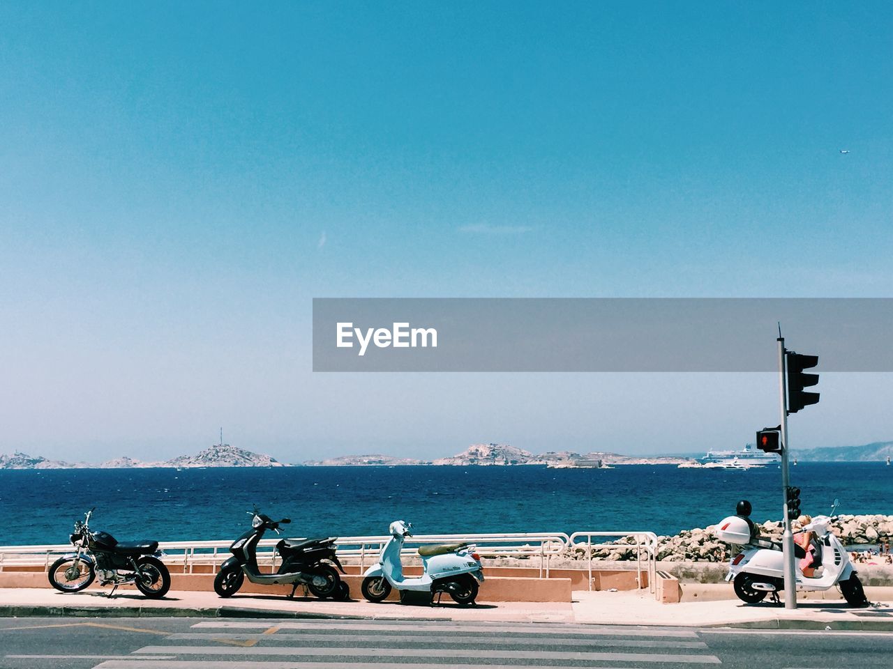 Motor scooters parked on sidewalk against blue sky