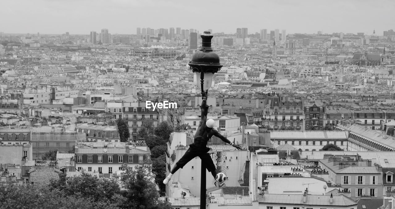 Street performer doing acrobatics on street light against cityscape