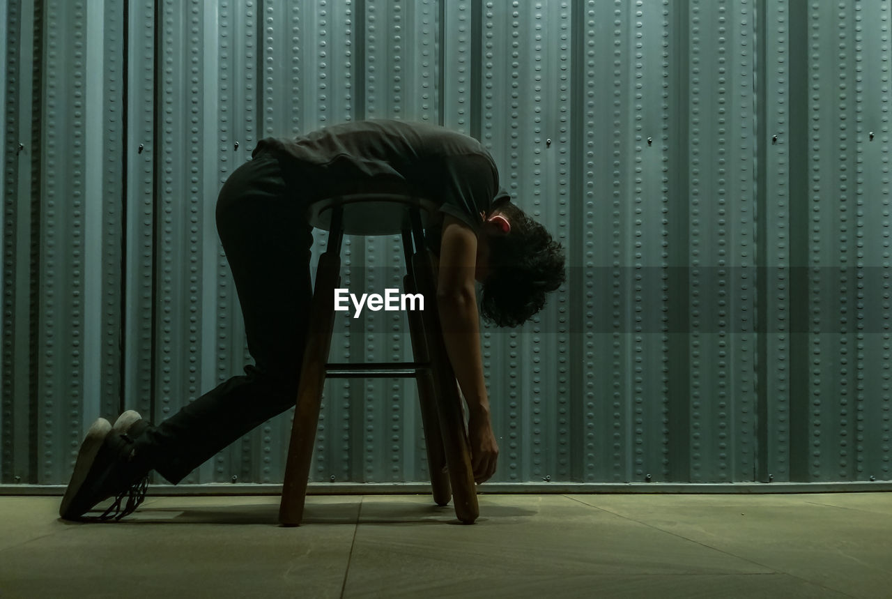 Young man lying on stool against wall