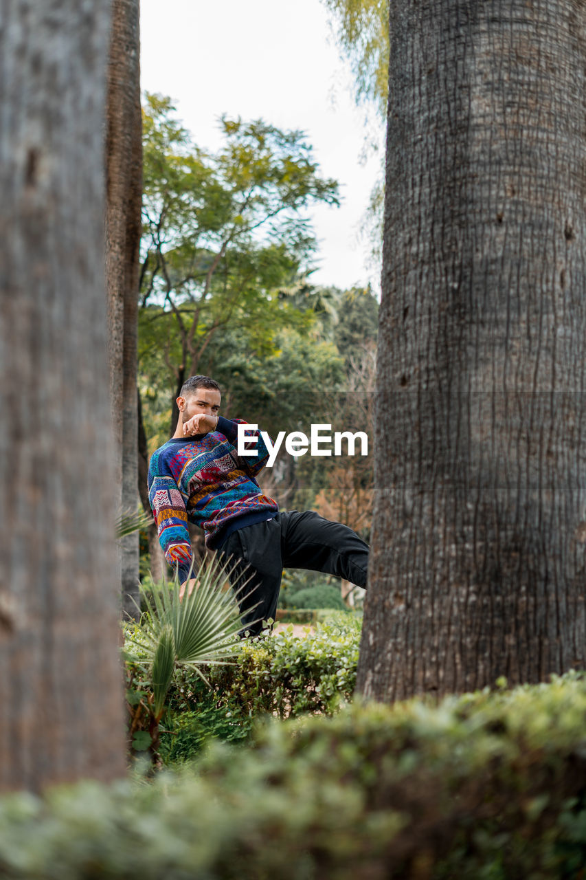 Caucasian model standing in between palm trees in a public park