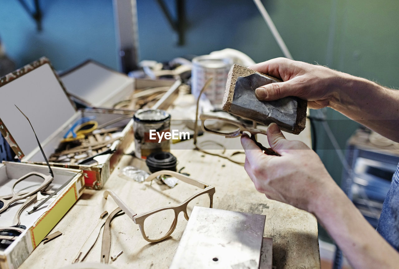 Cropped image of male owner rubbing eyeglasses with work tool at workshop