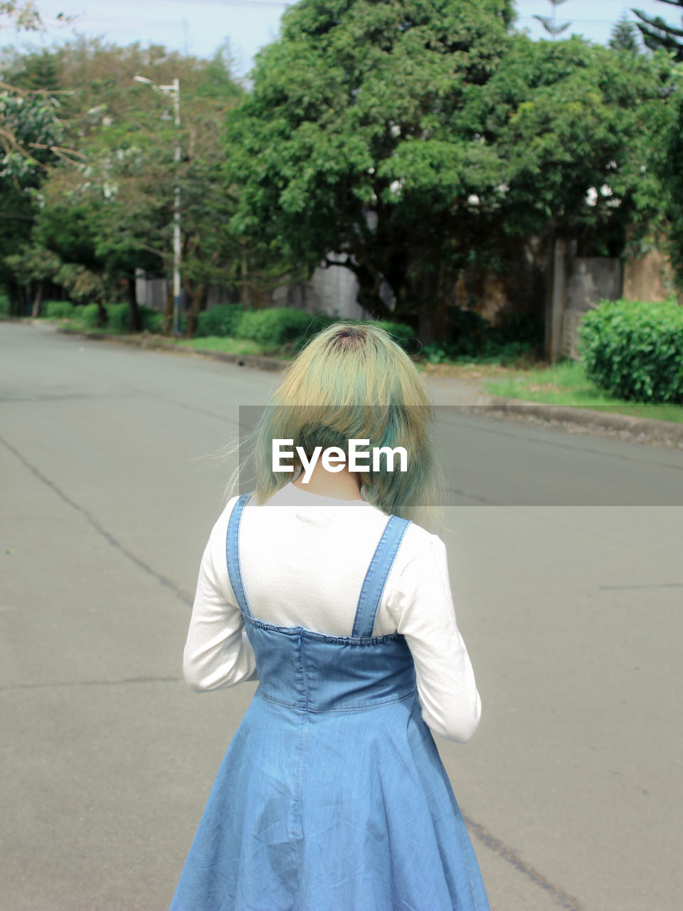 REAR VIEW OF WOMAN STANDING ON ROAD BY TREES