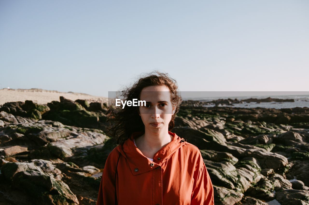 Portrait of young woman standing at beach against sky