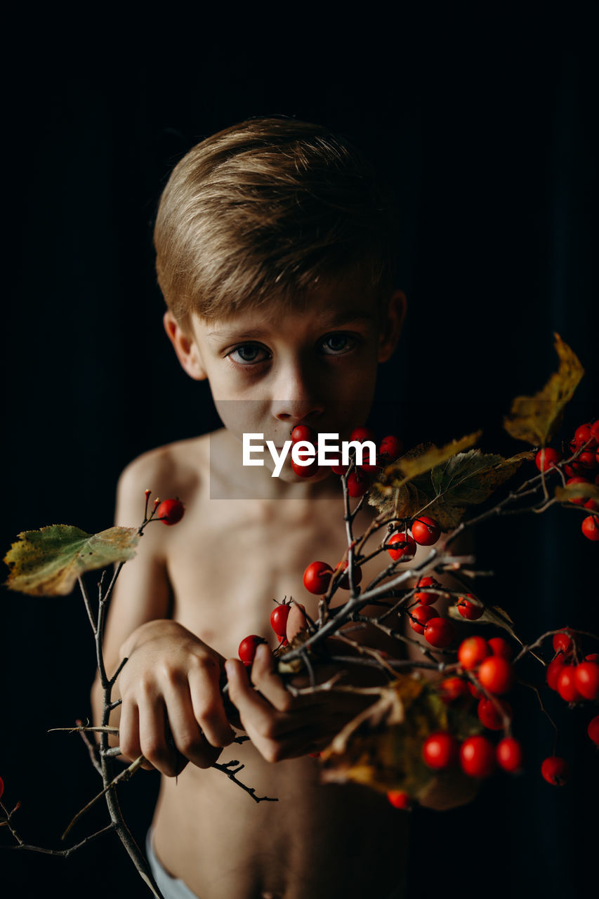 Portrait of boy holding berries against black background