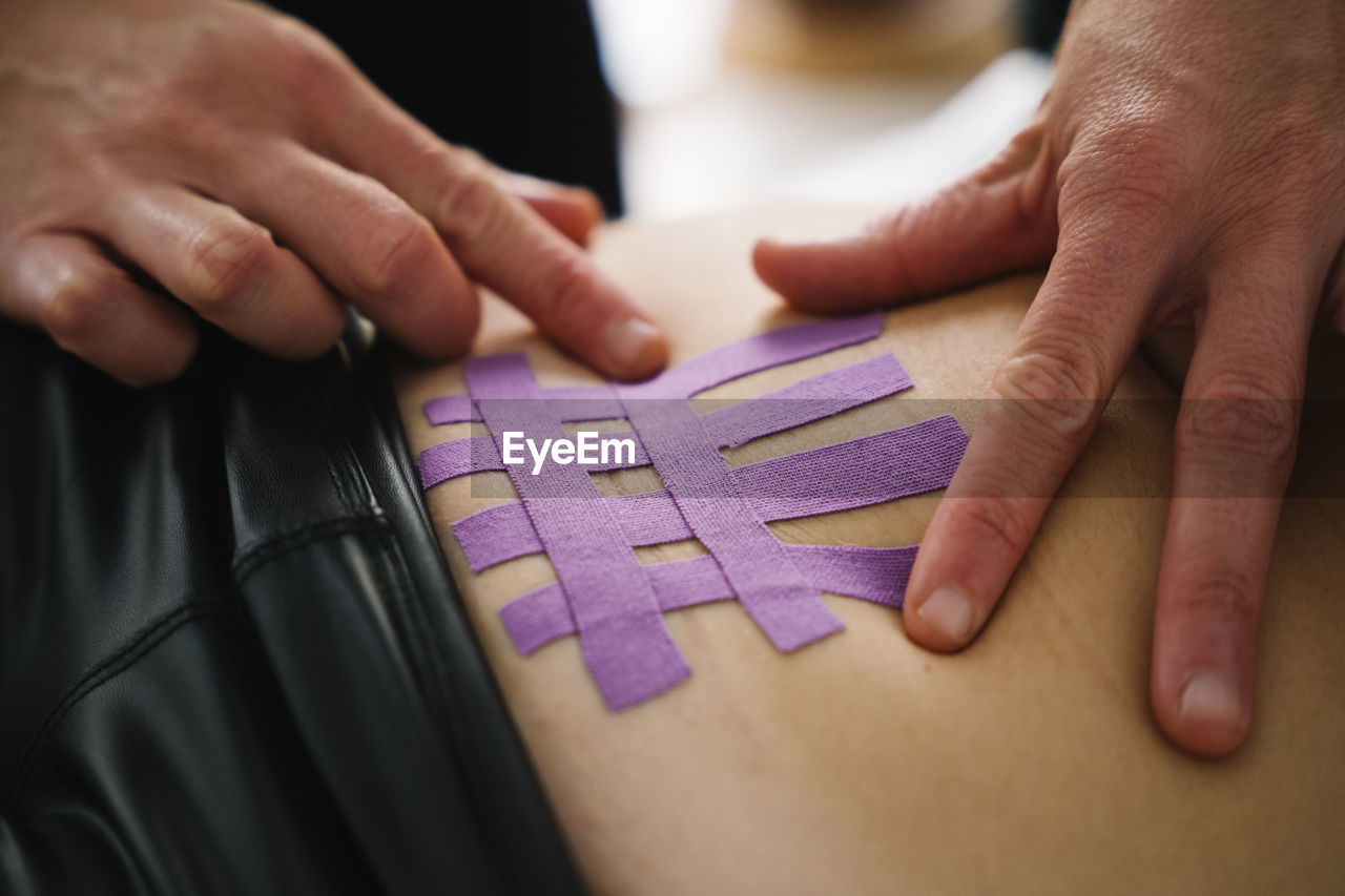 Female nurse applying purple elastic therapeutic tape on woman abdomen