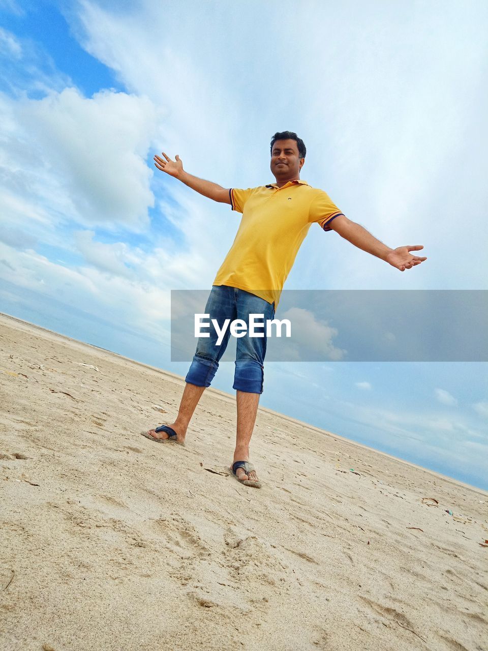 Portrait of man standing with arms outstretched at shore of beach against sky