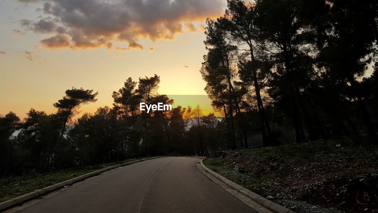 Road amidst trees against sky during sunset