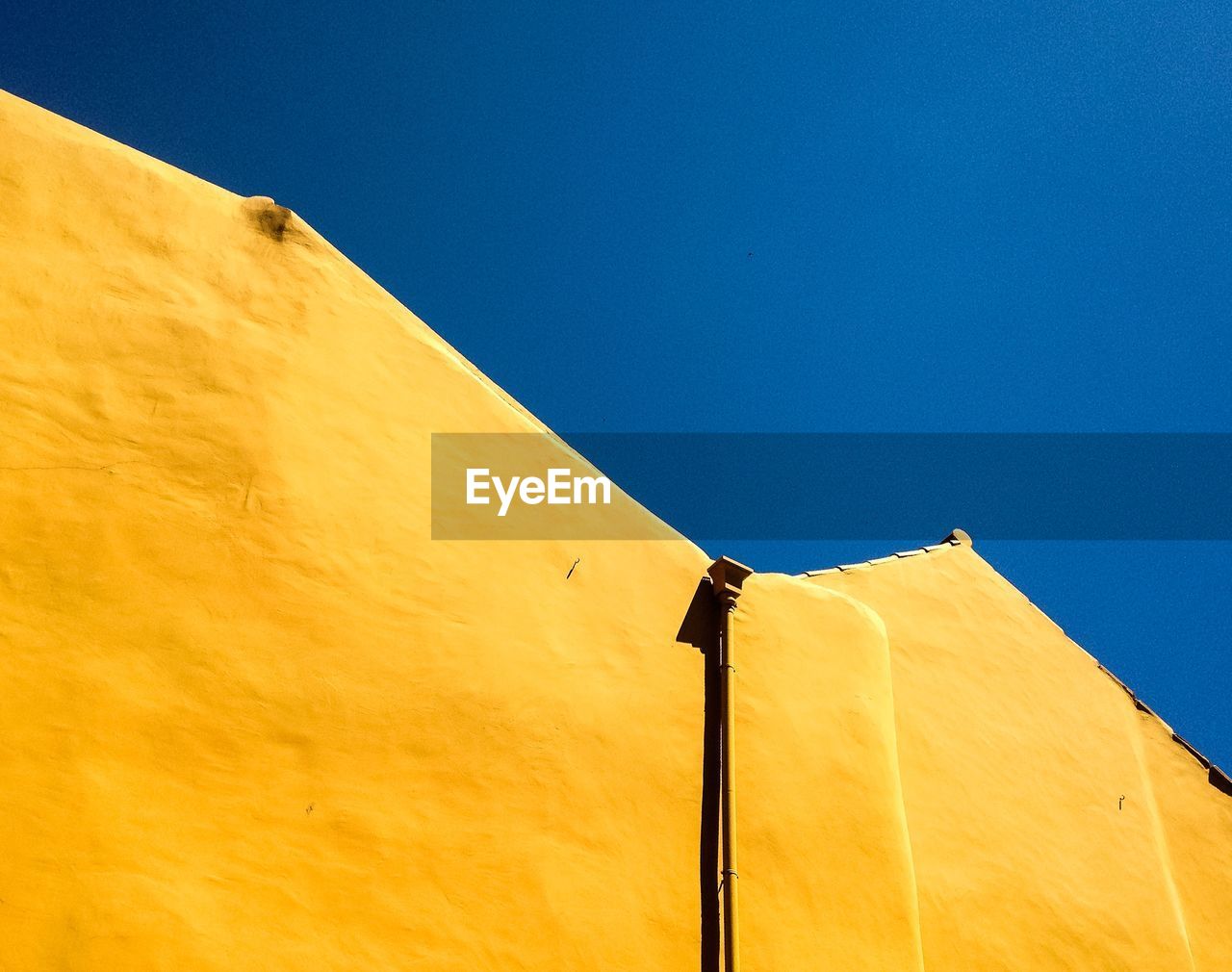 Low angle view of yellow building against clear blue sky