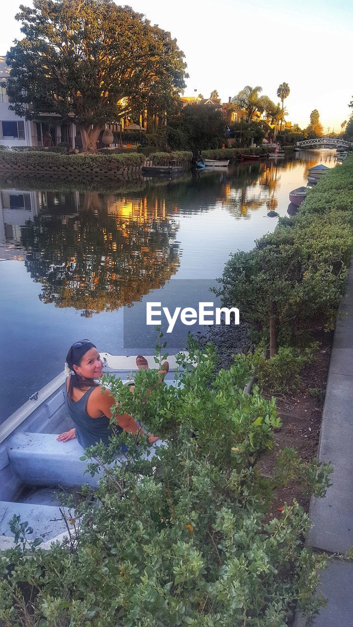 REAR VIEW OF WOMAN SITTING BY LAKE