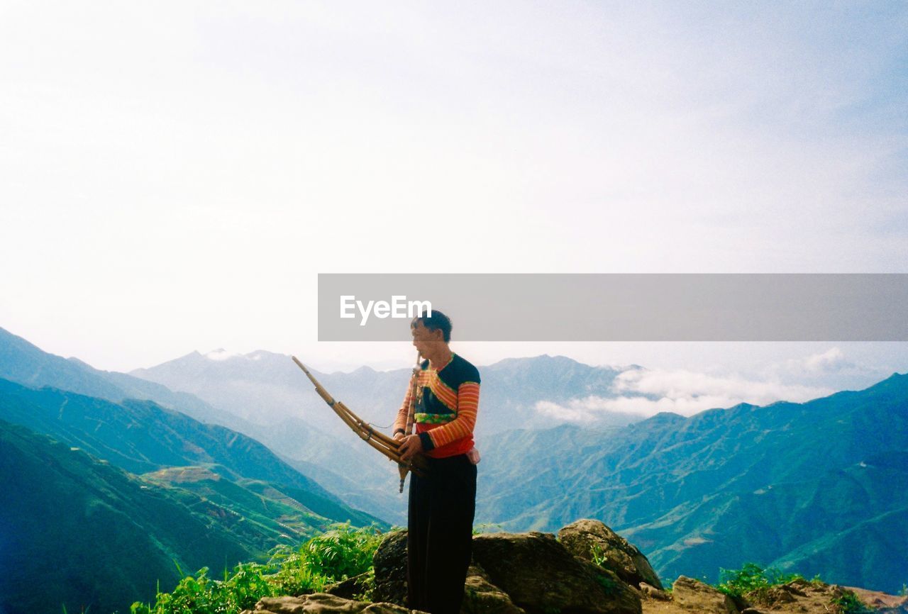 Side view of man standing on mountain against sky