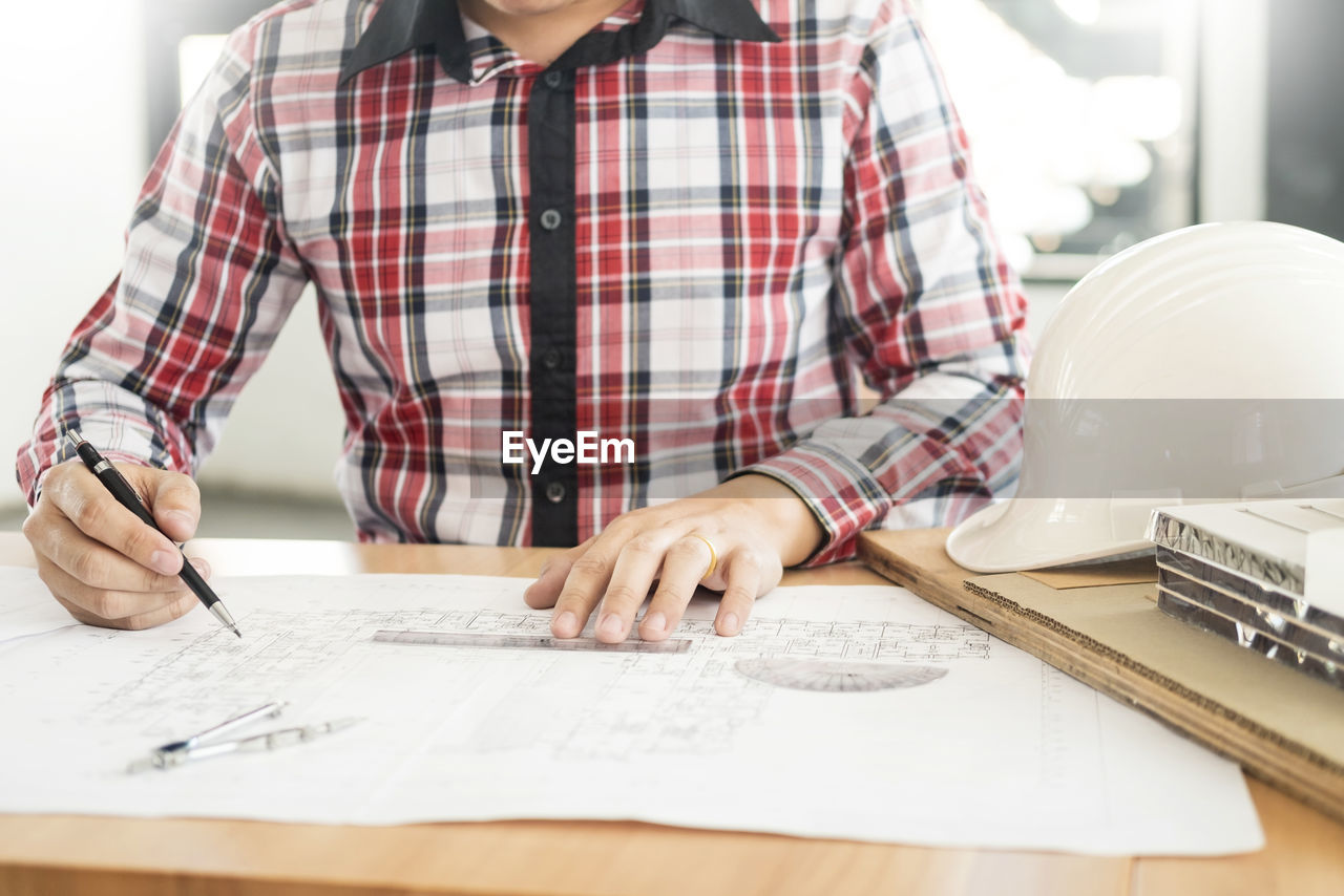 Midsection of engineer working on blueprint while sitting at table