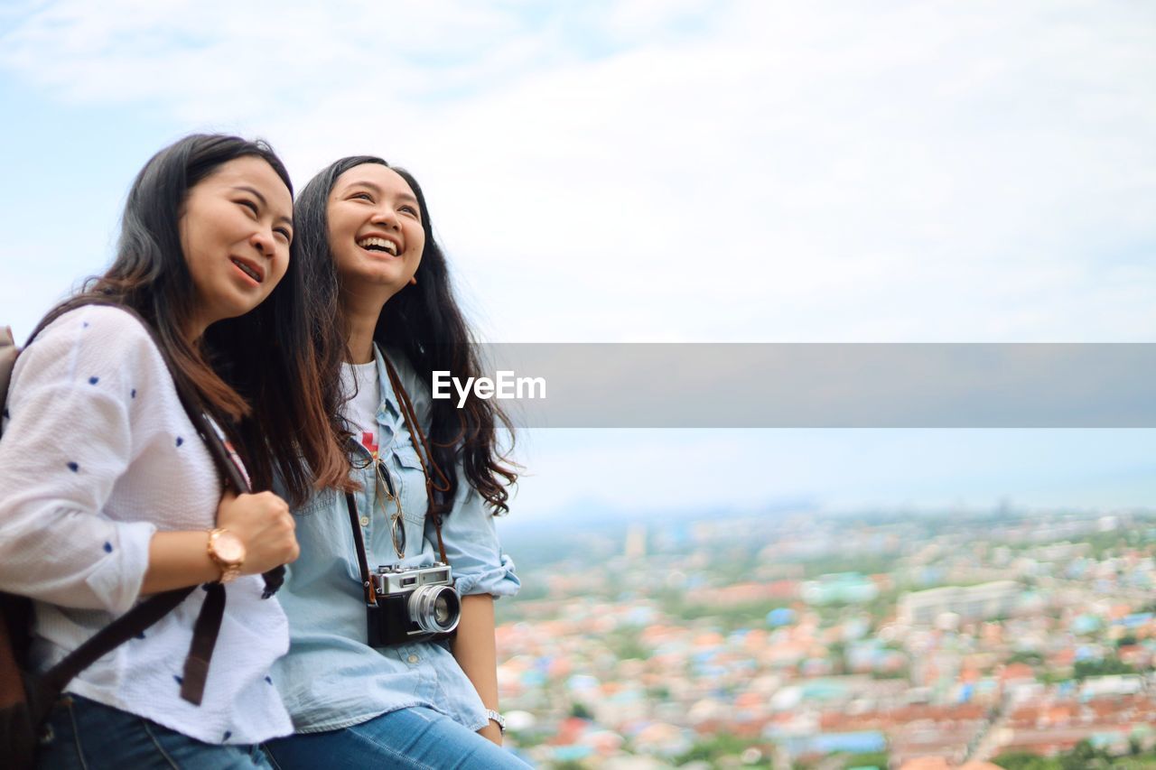 HAPPY YOUNG WOMAN SMILING IN CITY AGAINST SKY IN BACKGROUND