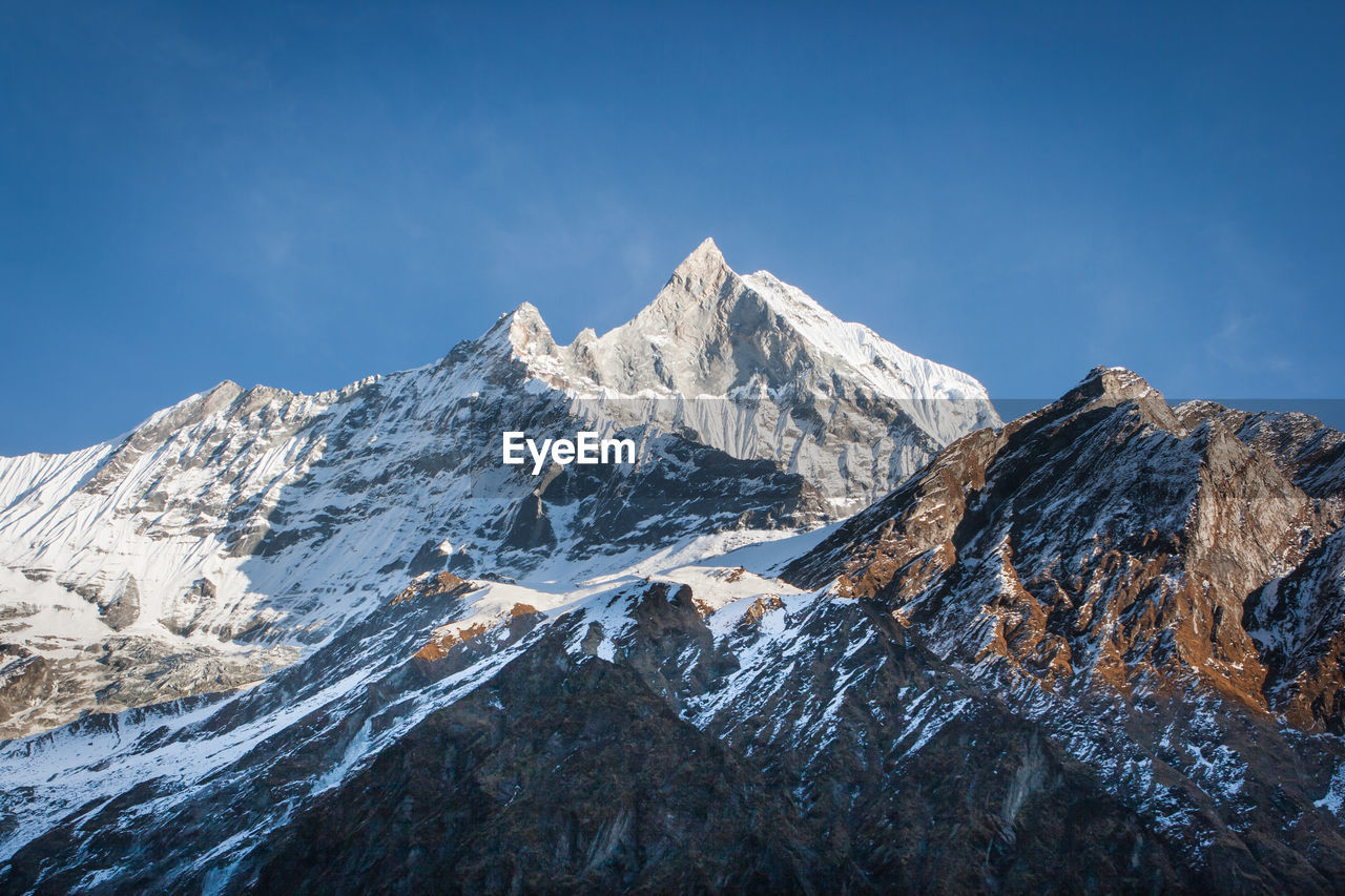 Low angle view of snowcapped mountains against clear blue sky