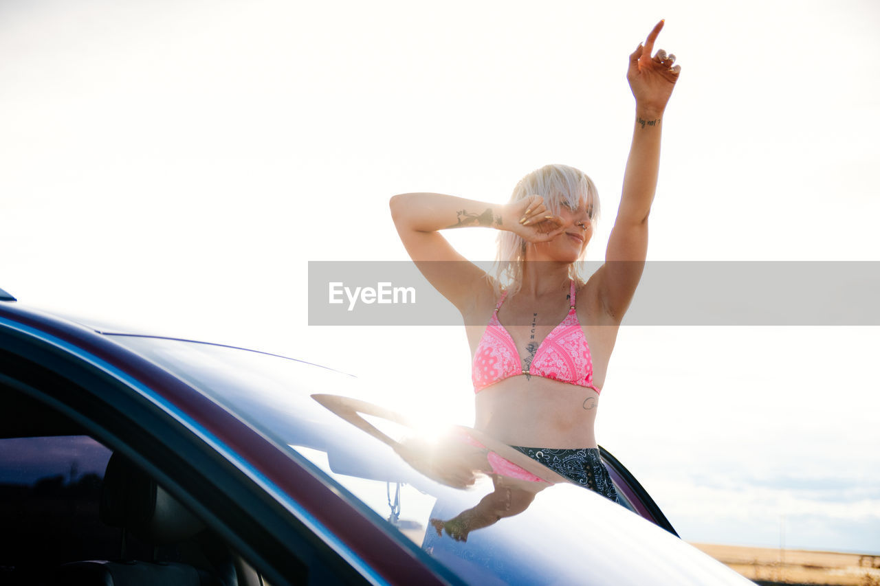 Young woman dancing outside her car in a bikini in the sun