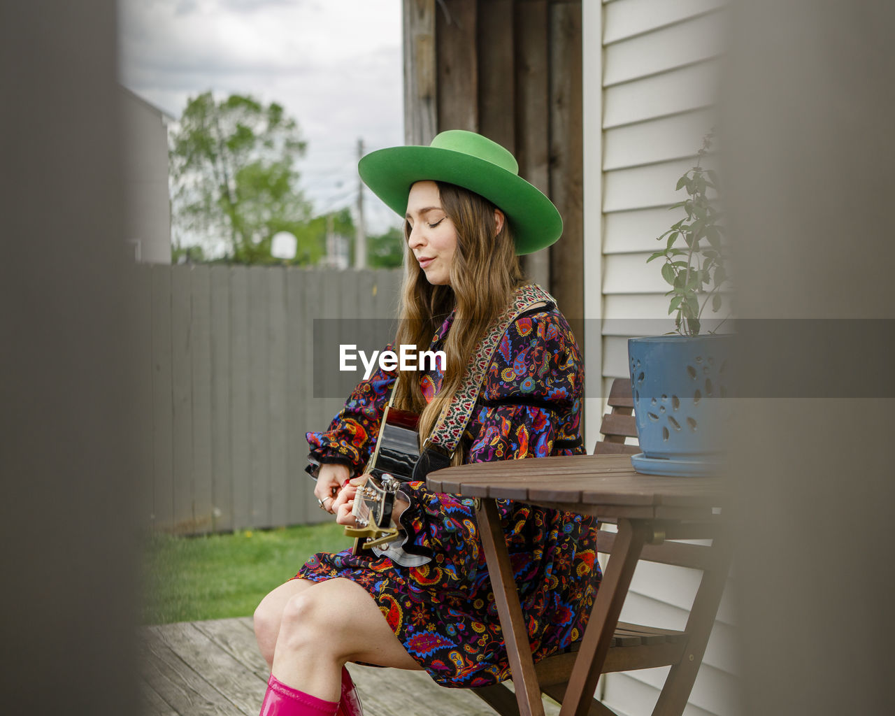 Side-view of a woman with eyes closed sitting on porch playing guitar