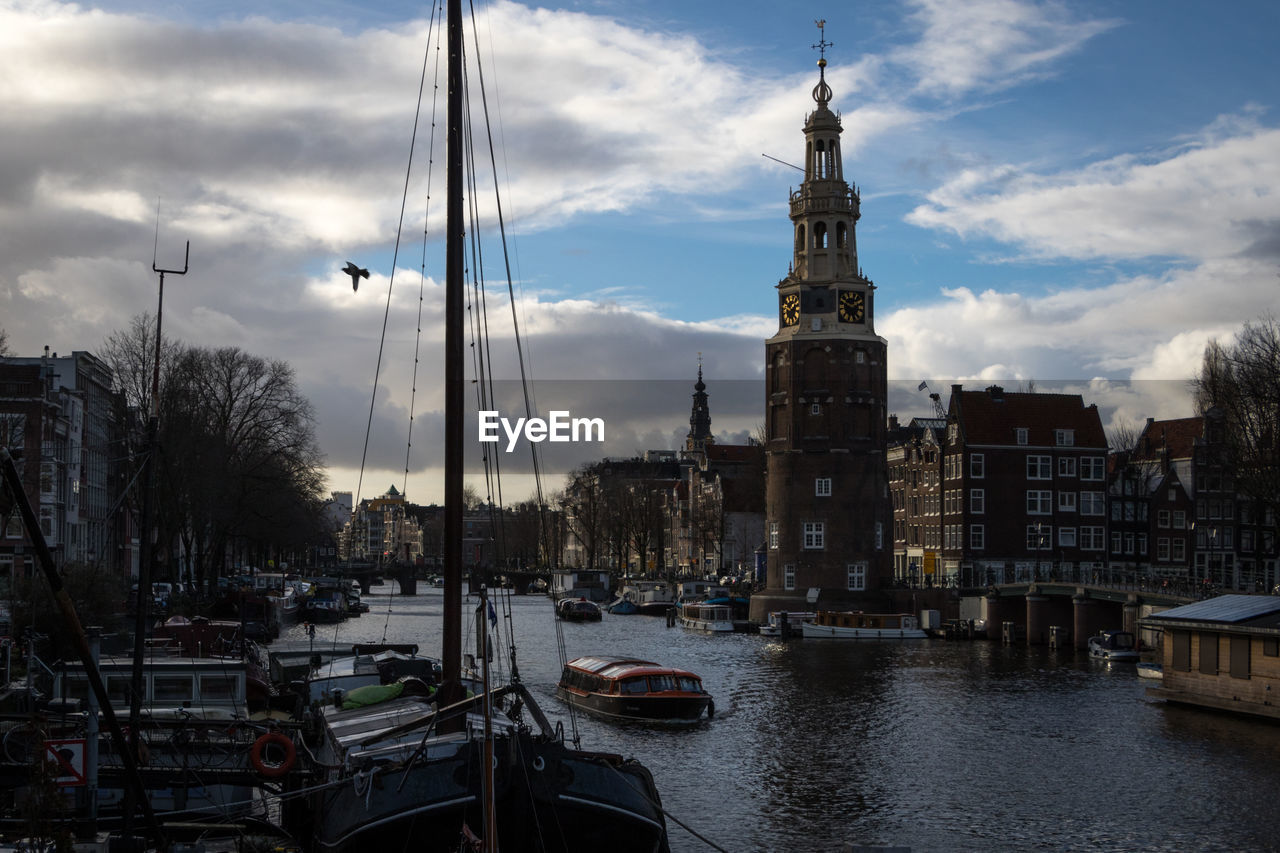 Sailboats moored on river by buildings in city against sky