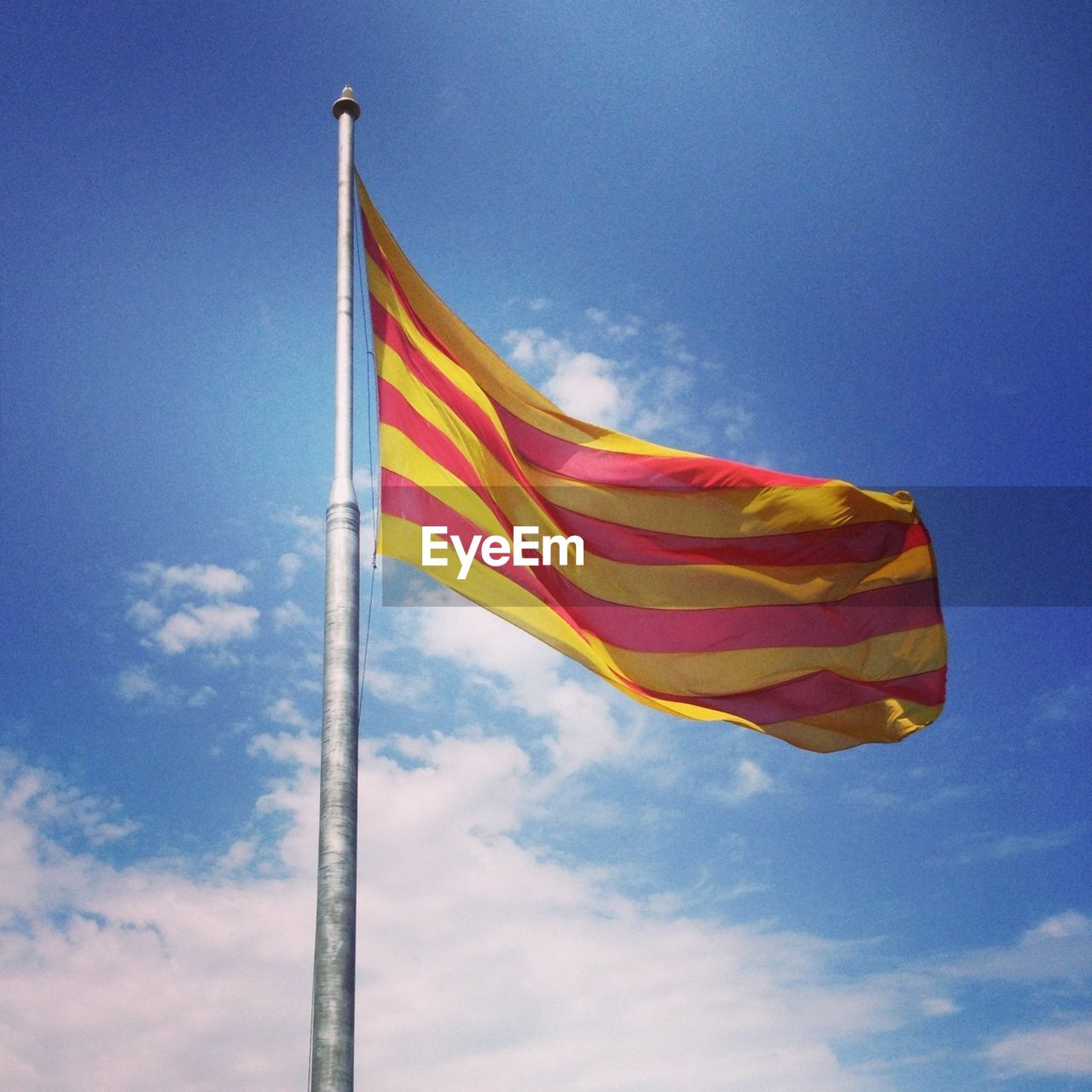 Low angle view of catalonia flag fluttering against blue sky and clouds