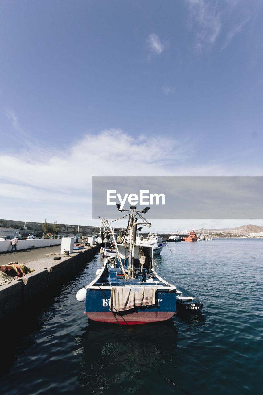 FISHING BOAT MOORED AT HARBOR AGAINST BLUE SKY