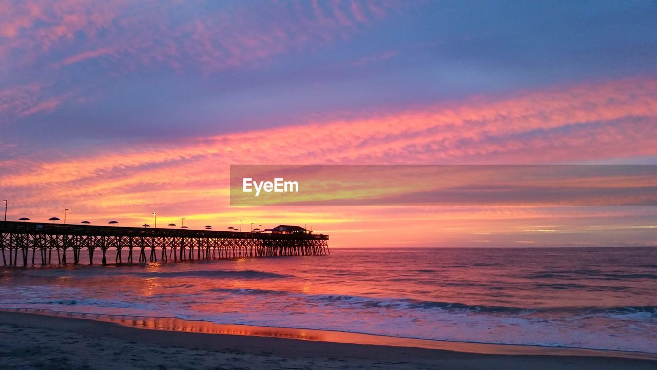 Pier at beach against sky during sunset