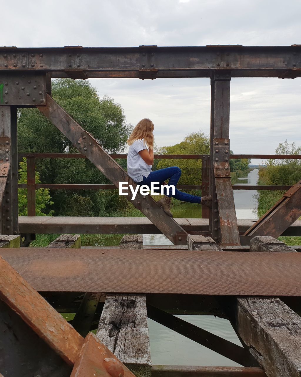 Woman sitting on bridge against sky