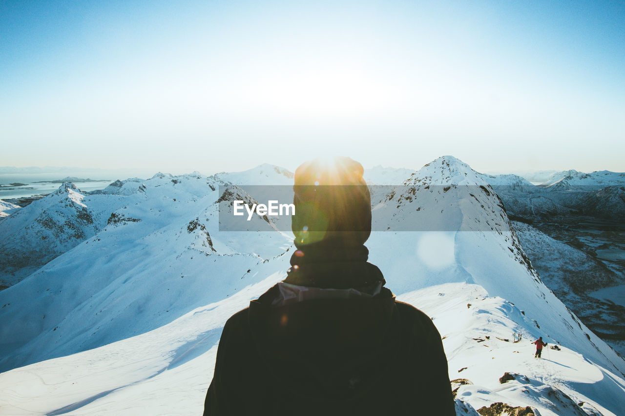 REAR VIEW OF WOMAN ON SNOWCAPPED MOUNTAIN AGAINST SKY