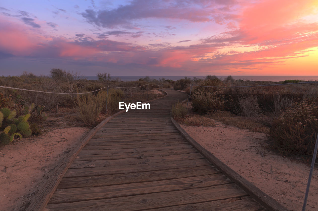 Boardwalk against sky during sunset