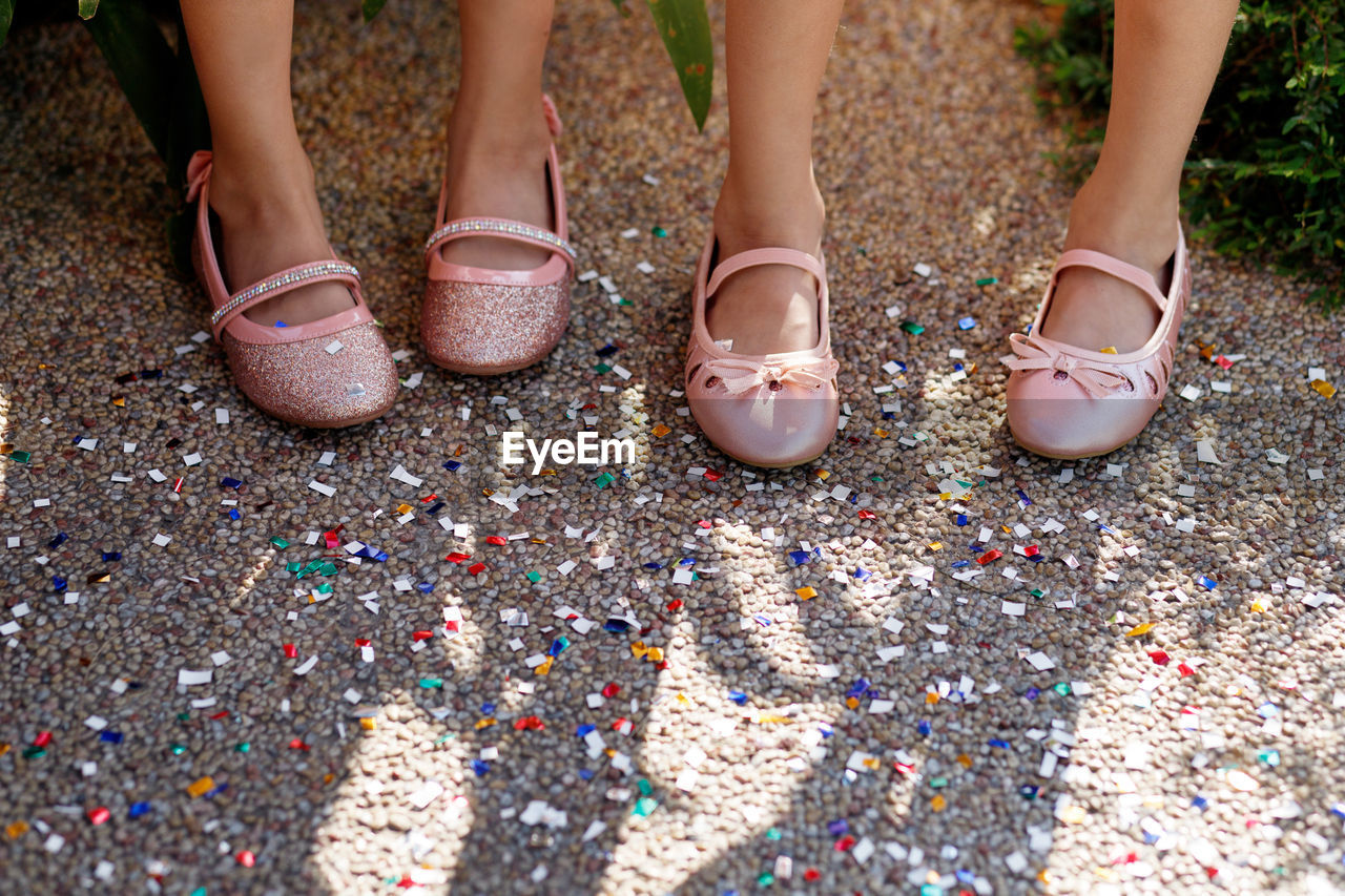 Low section of female friends wearing shoes while standing on colorful confetti