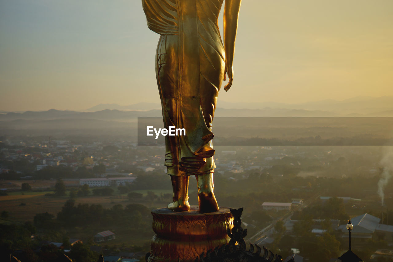 Statue of budda against buildings in city at sunset