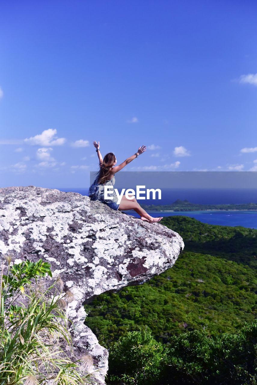 Woman standing on rock by sea against sky