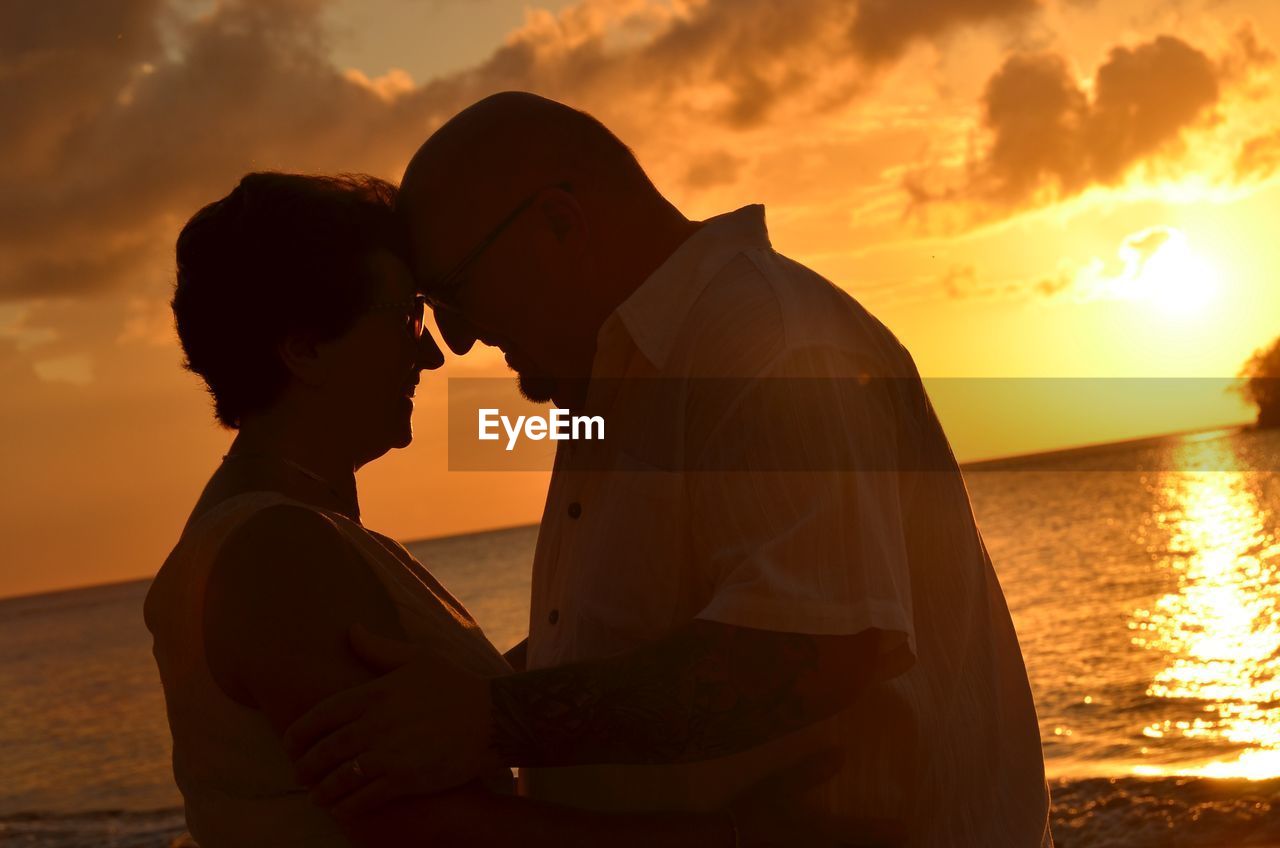 Side view of romantic couple looking at each other against sea during sunset