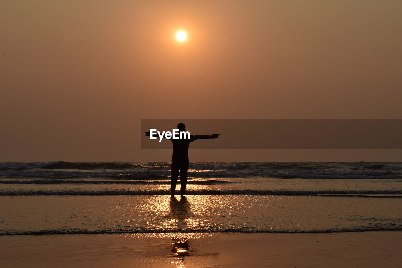 Silhouette man standing in sea against sky during sunset