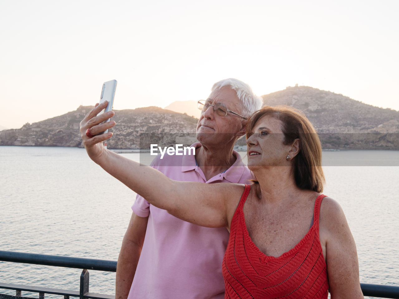 Relaxed senior couple taking a selfie to remember with the seaport beh