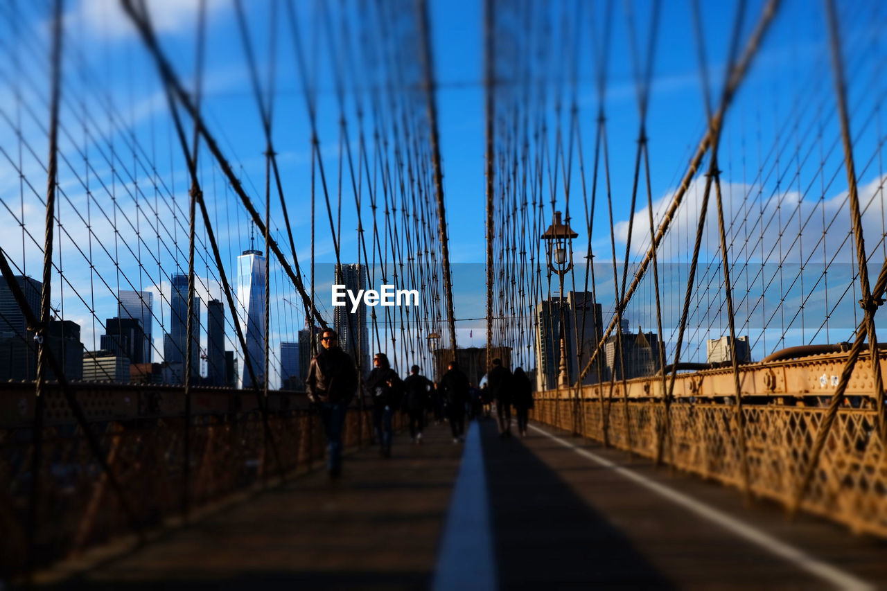 PEOPLE WALKING ON SUSPENSION BRIDGE AGAINST SKY