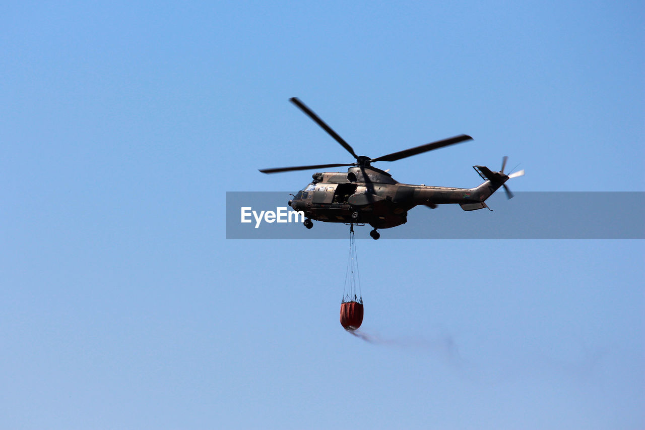 Low angle view of helicopter against clear blue sky