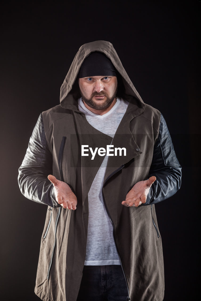 Portrait of hipster man gesturing while standing against black background