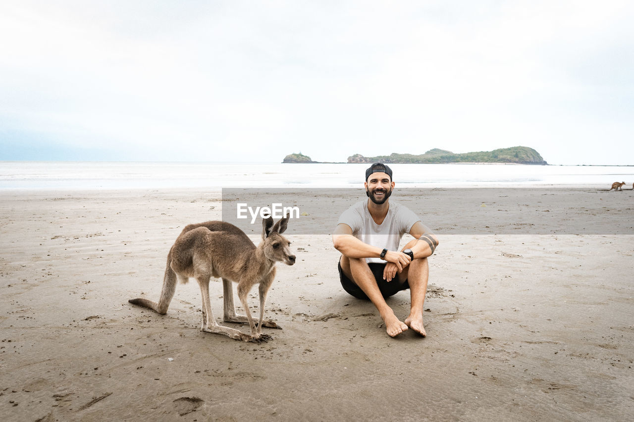 Full length of young man with kangaroo sitting at beach