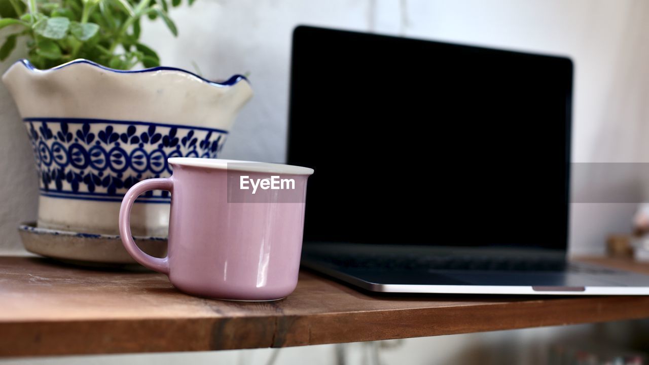 Close-up of coffee cup on table with laptop