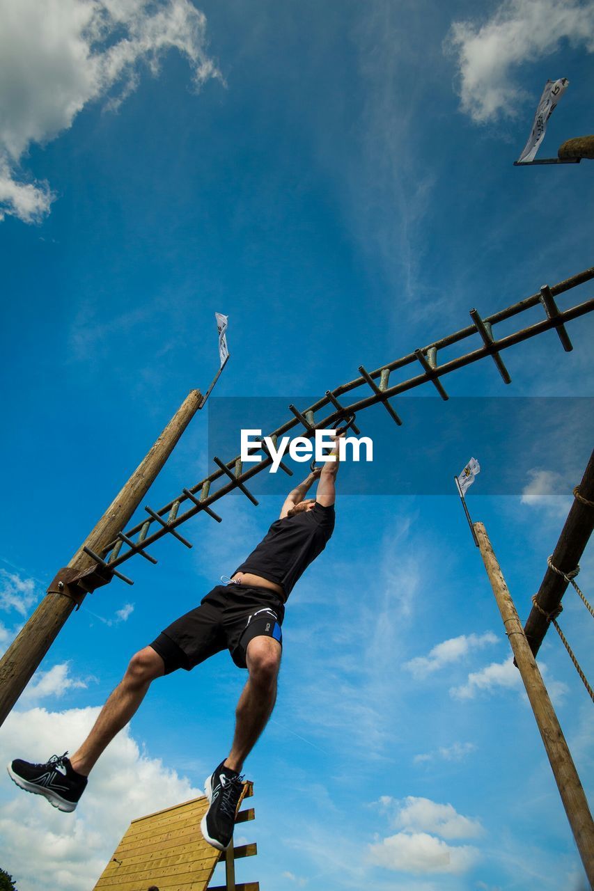 Low angle view of man hanging on structure against sky