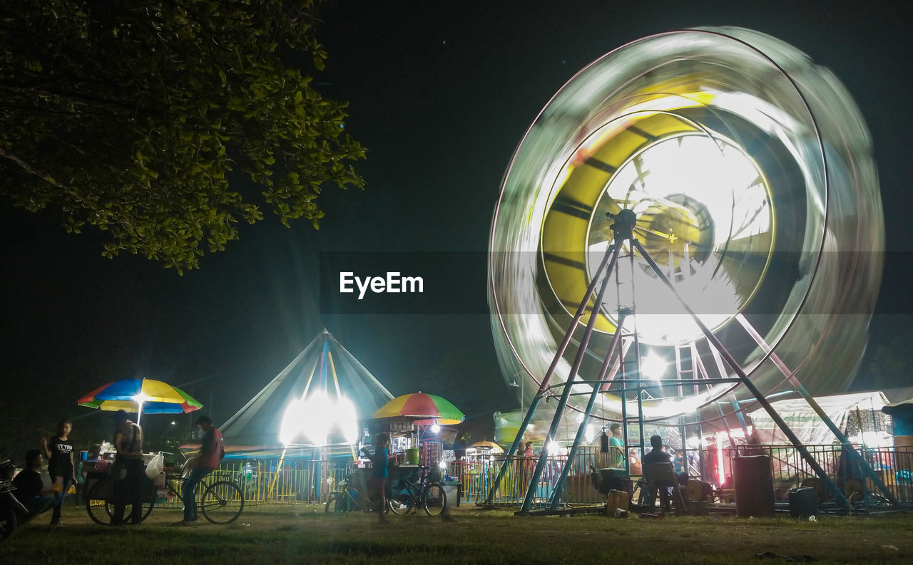 PEOPLE AT AMUSEMENT PARK RIDE AT NIGHT