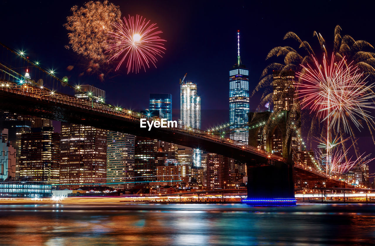 FIREWORK DISPLAY OVER RIVER BY BUILDINGS AT NIGHT