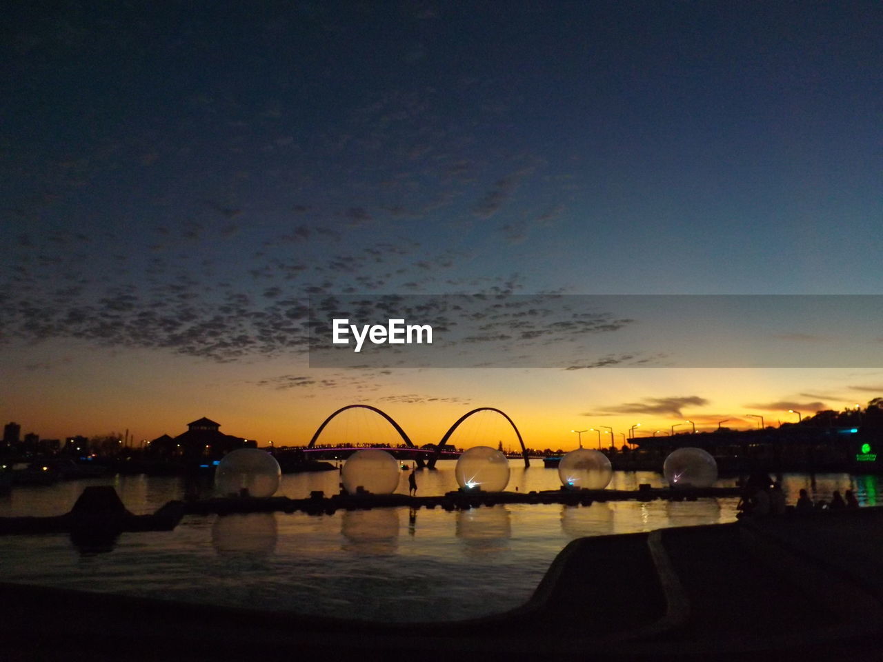 SILHOUETTE OF BRIDGE IN FRONT OF LAKE AT DUSK