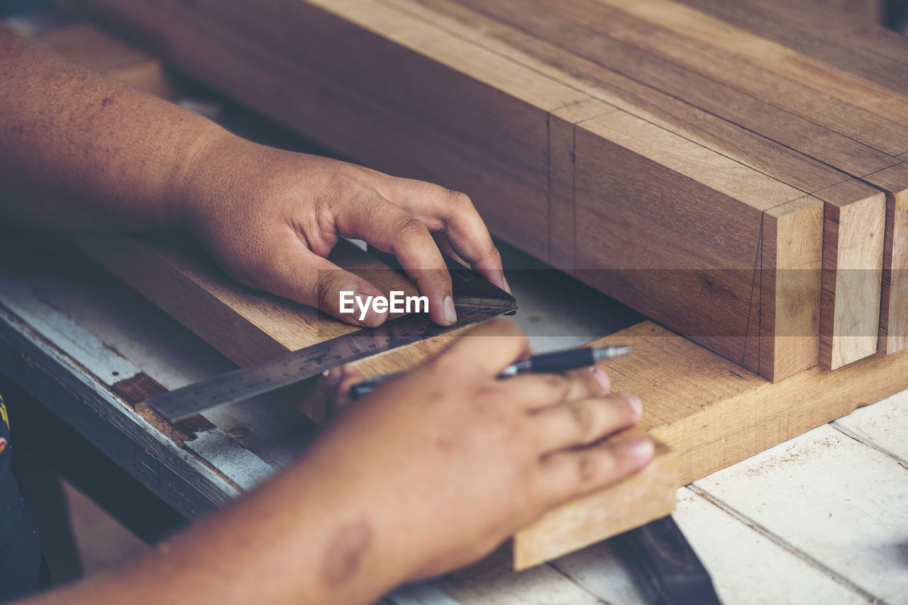 Cropped hands of male carpenter marking on wood in workshop