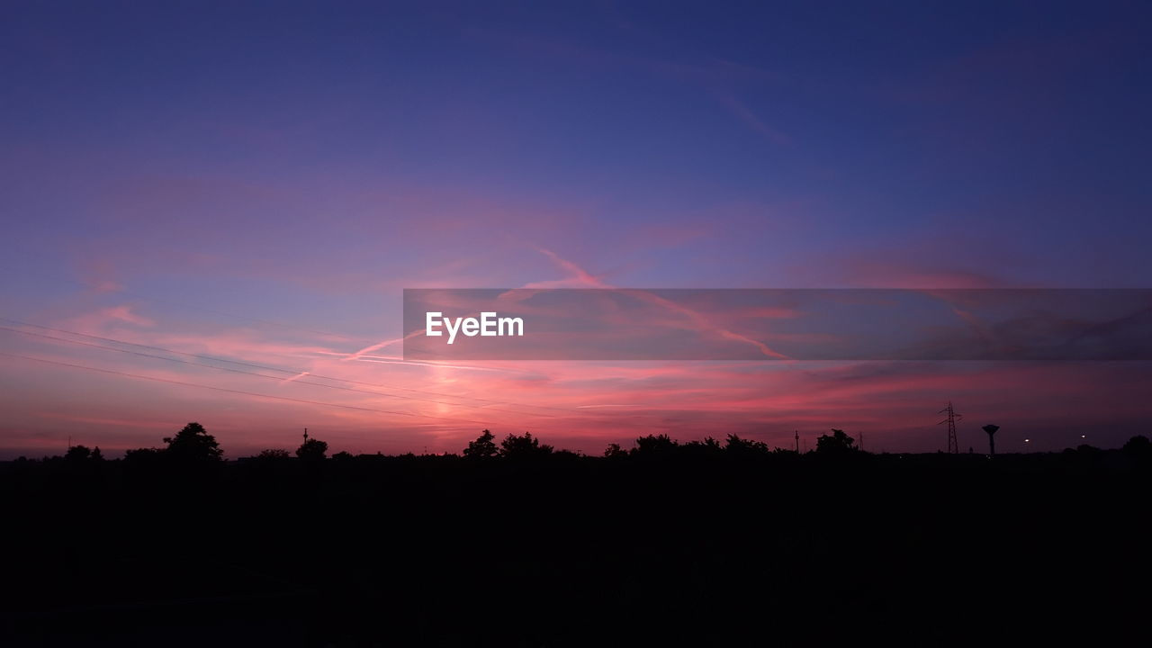 Silhouette trees against dramatic sky during sunset