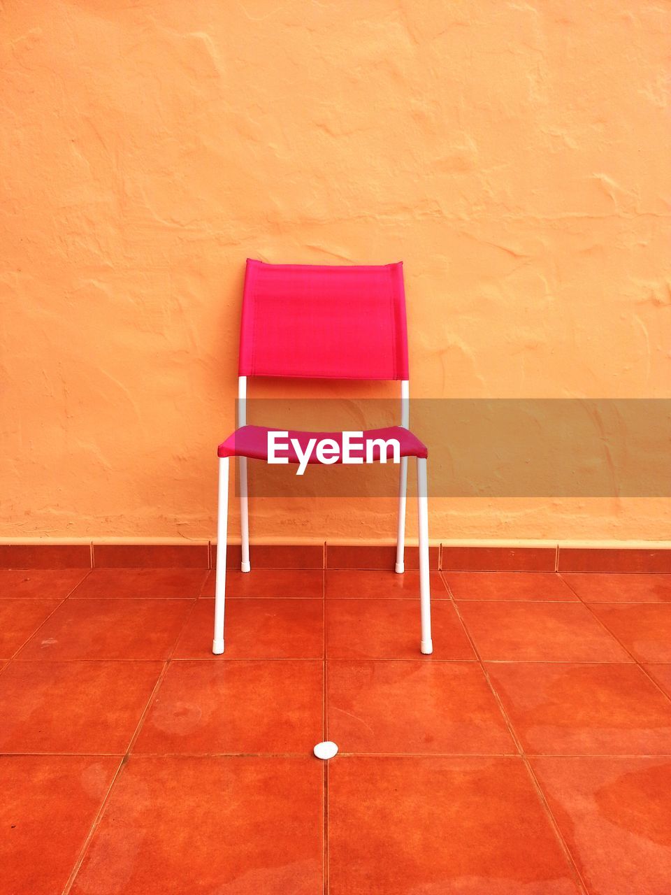 Empty pink chair on tiled floor against orange wall at home