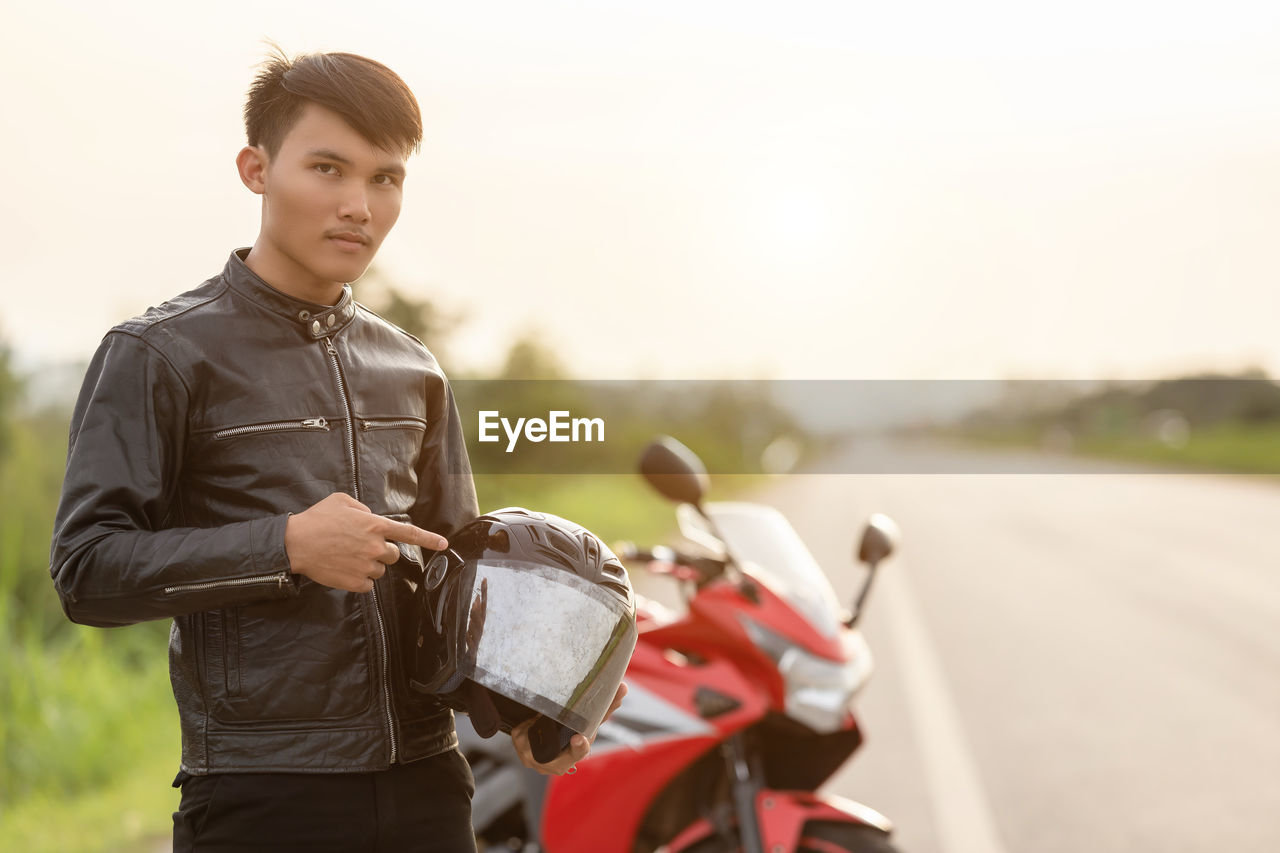 Portrait of young man standing by motorcycle on road