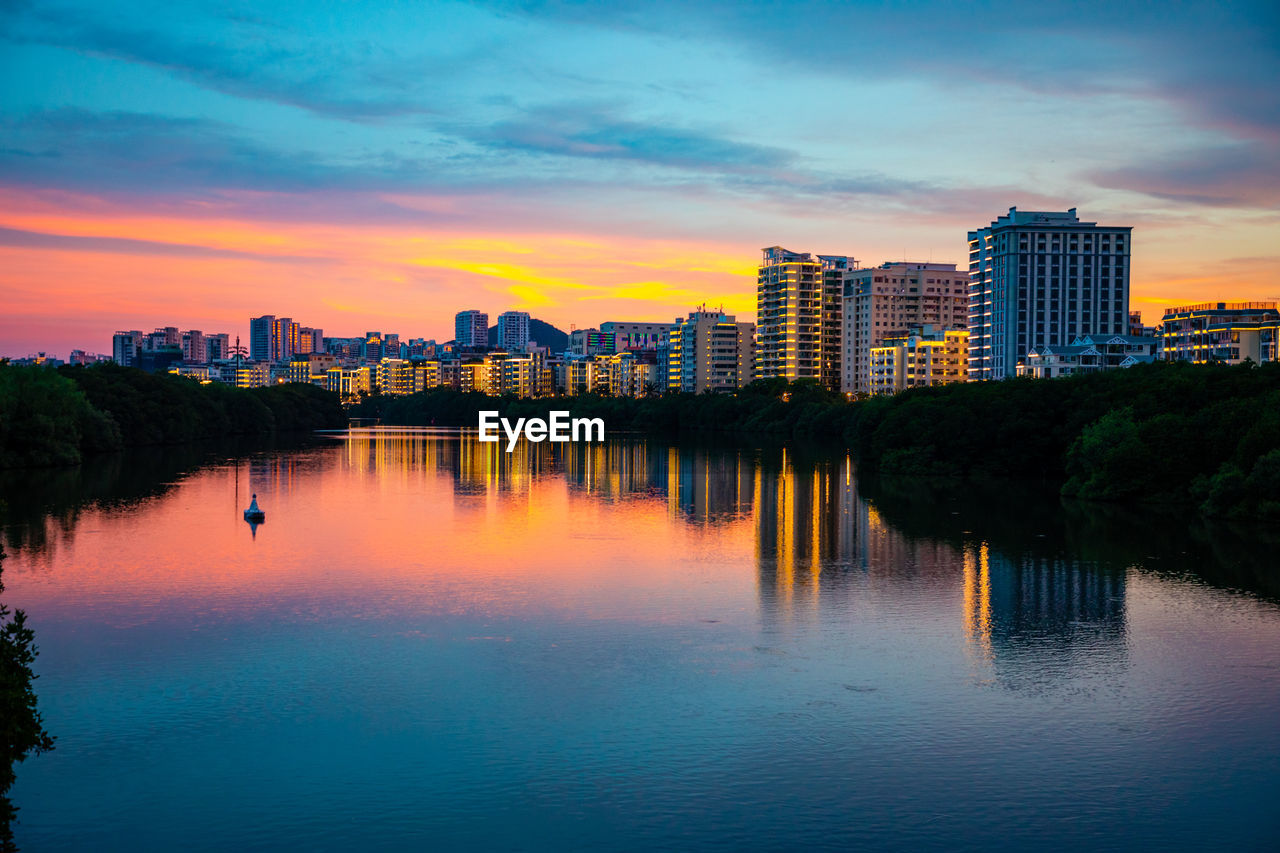 Lake and buildings against sky at sunset