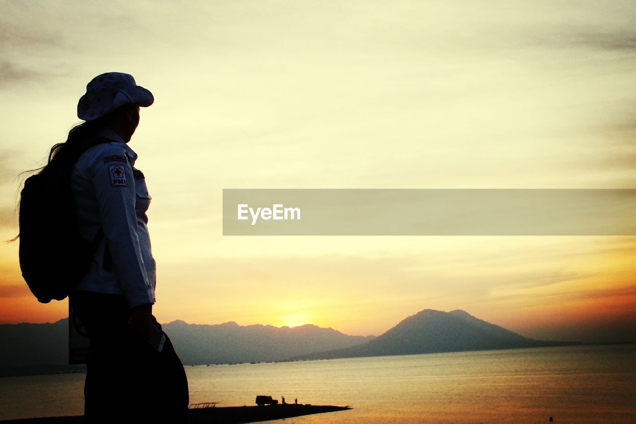 Side view of silhouette mature woman standing by sea against sky during sunset