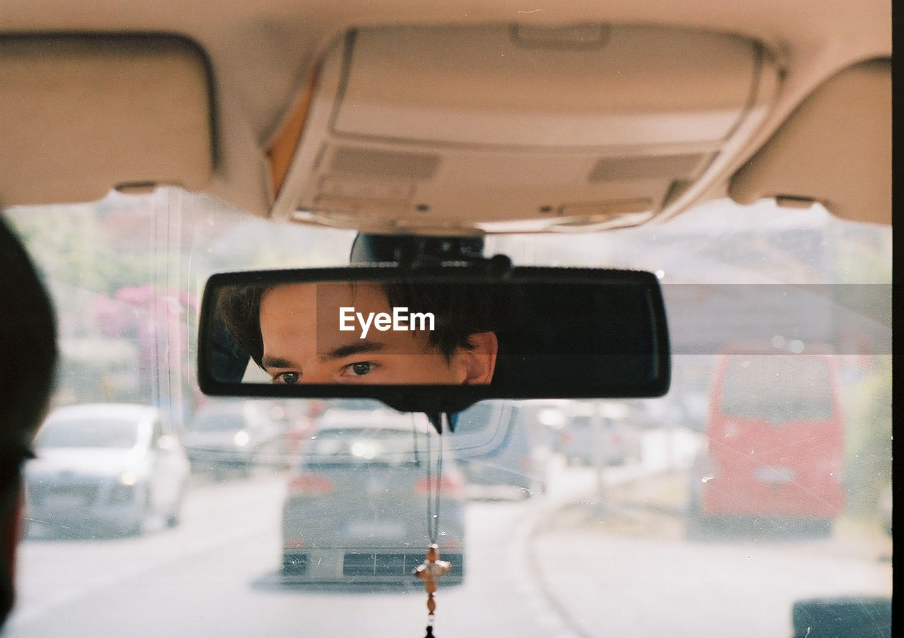 Eyes of a young man in the rear-view mirror of a car