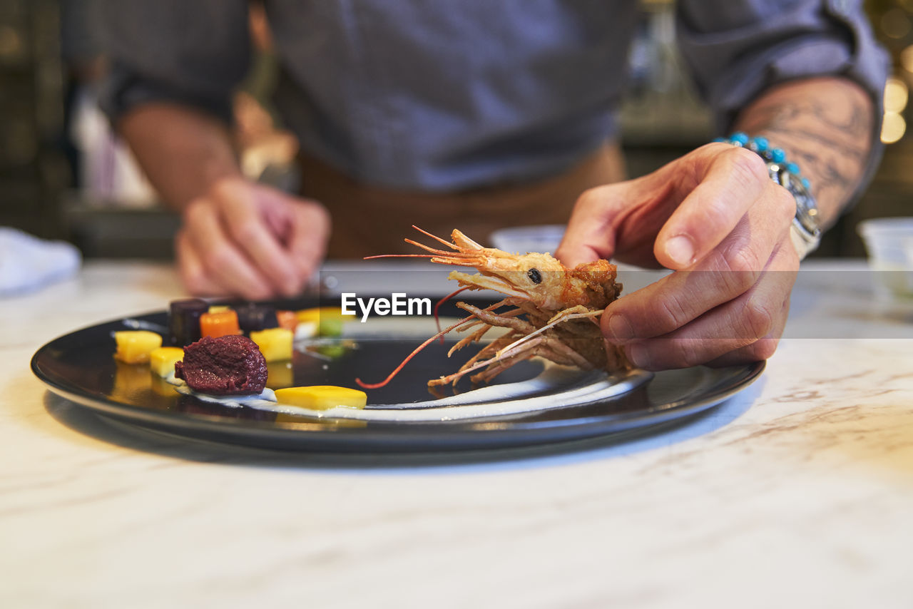 Crop anonymous chef with tongs arranging colorful edible blossoms on plate while garnishing sophisticated dish in restaurant kitchen